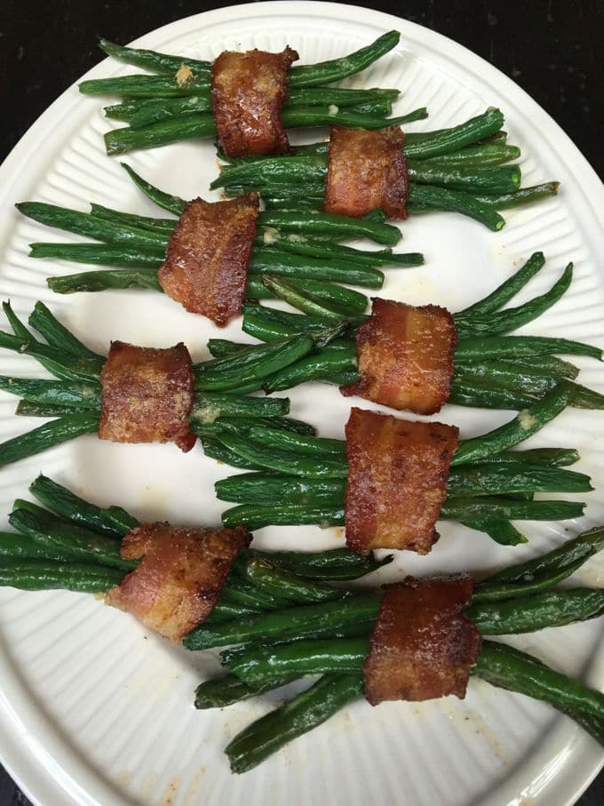 Eight bundles of green beans wrapped in bacon on a white serving dish.
