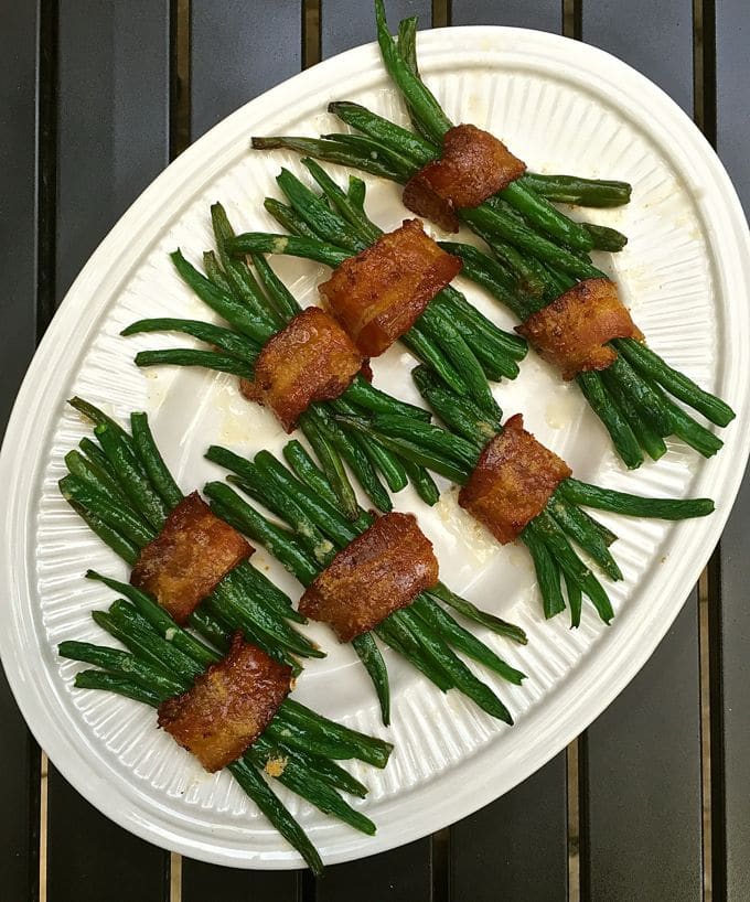 Cooked green beans wrapped in bacon on a white serving platter