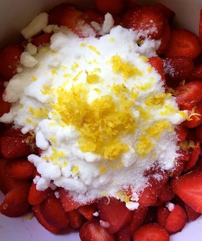 Sugar and lemon zest for on top of sliced strawberries in a bowl.