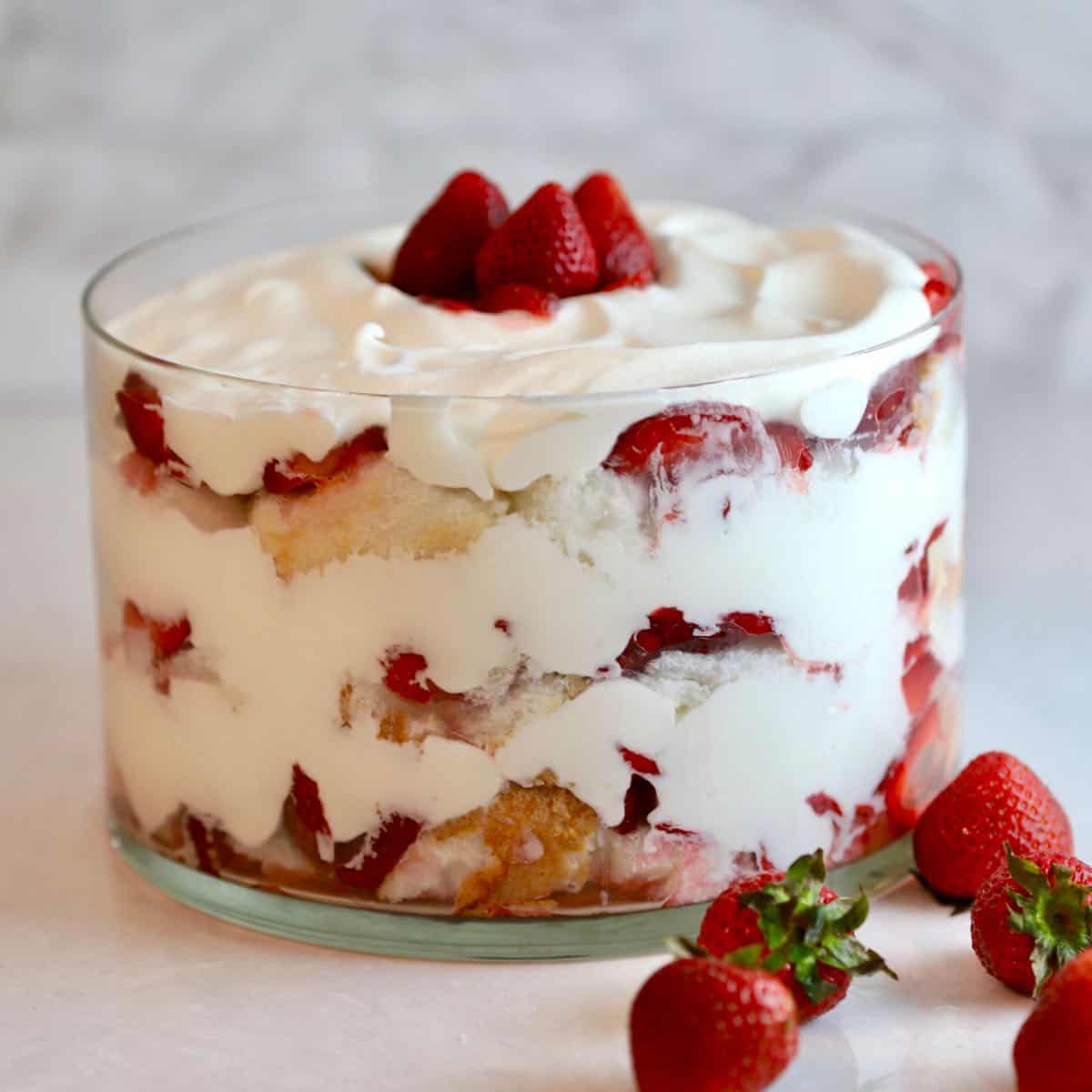 A clear glass trifle dish with layers of strawberries, angel food cake and whipped cream. 