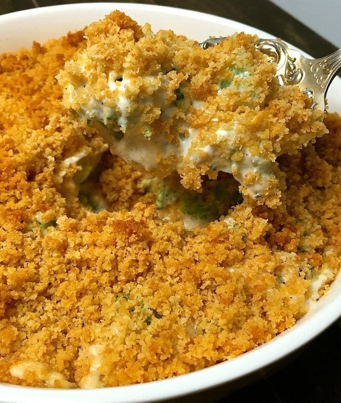 A spoonful of Broccoli Cheese Casserole taken out of a round white bowl.