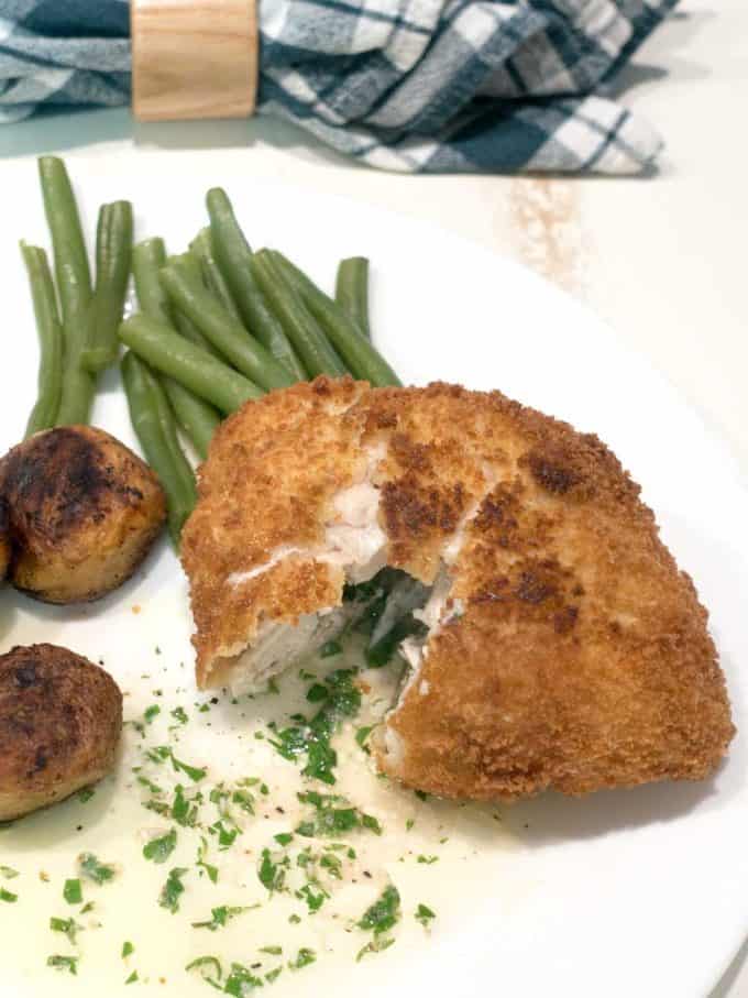 Chicken Kiev on a white plate with green beans and small potatoes. 