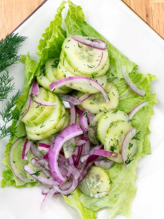 A sliced cucumber, onion and dill salad on a square white plate.