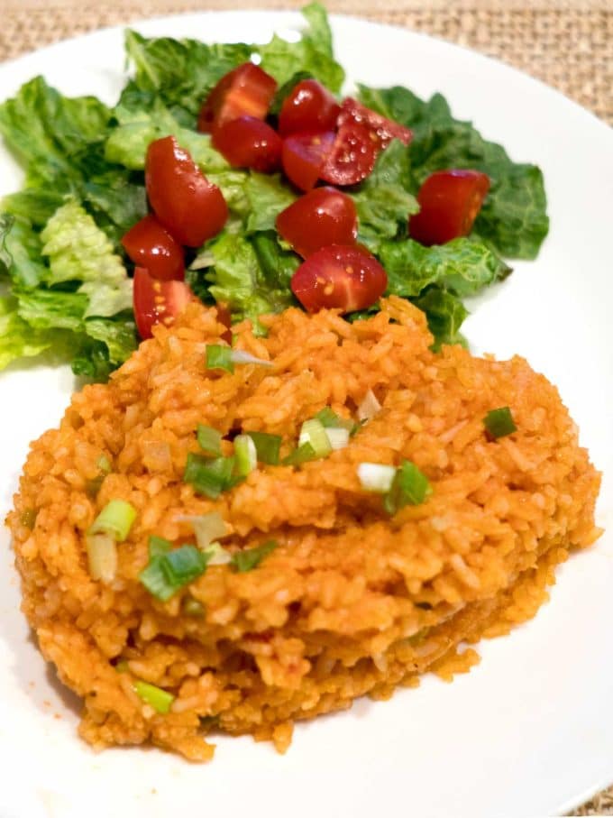 Mexican Rice topped with chopped scallions on a plate with a side salad