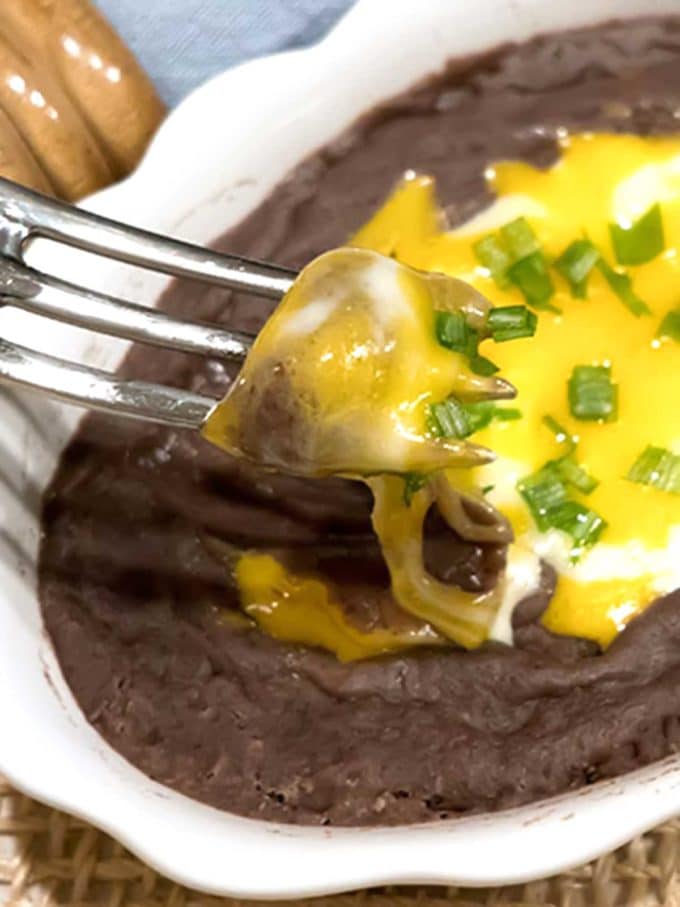 Mexican Smashed Black Beans on a plate topped with melted cheese and chopped chives