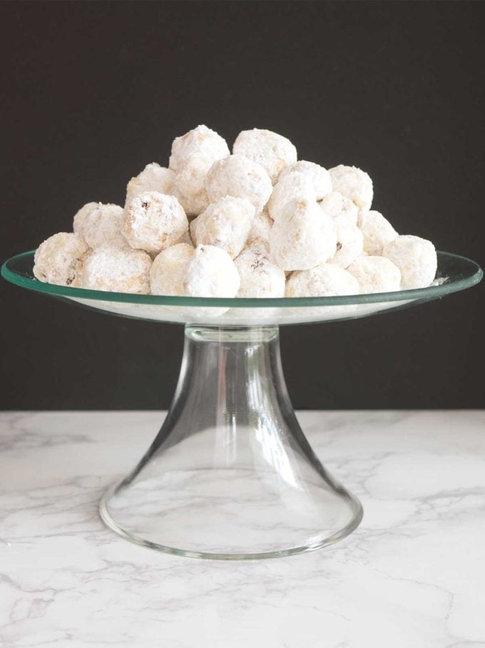 A clear glass serving dish full of Mexican Wedding Cookies covered with powdered sugar