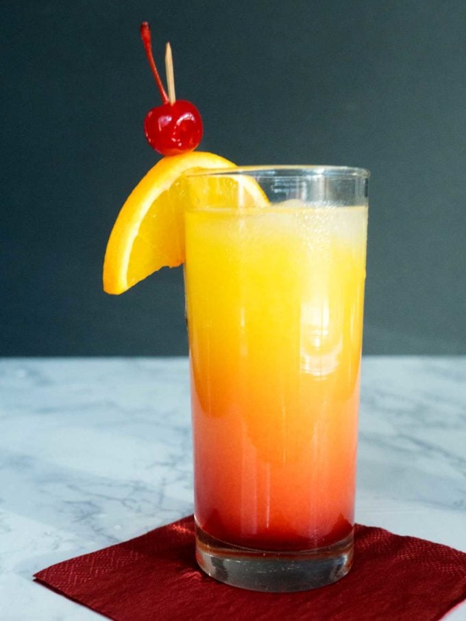 Tequila Sunrise for Cinco de Mayo in a tall glass garnished with orange slices and a cherry