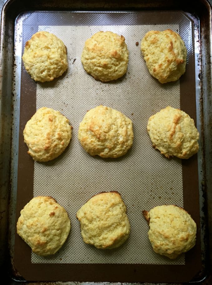 Nine cooked drop biscuits on a silicone baking mat. 