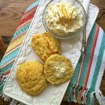 A plate of cornmeal biscuits and a small bowl of orange butter.