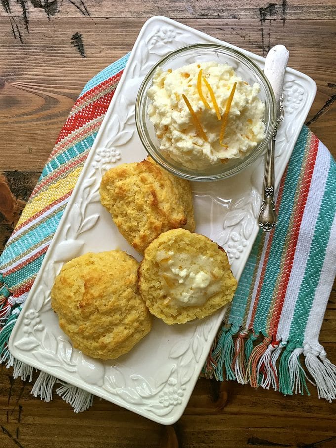 A white serving plate with biscuits and butter topped with orange zest. 