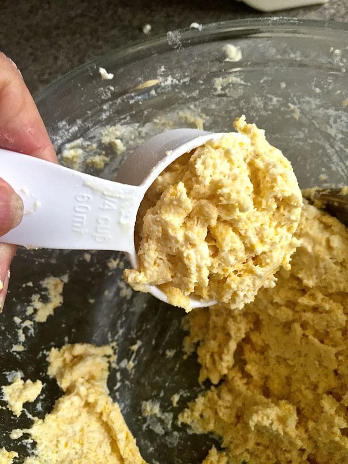 A plastic measuring cup with a scoop of cornmeal biscuit batter. 