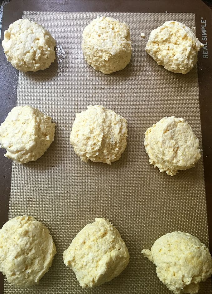 Nine uncooked cornmeal biscuits on a silicone baking mat. 