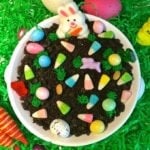 Easter Chocolate Cheesecake Dip in a small serving dish topped with crushed Oreos and decorated with an assortment of Easter candy sitting on easter grass.