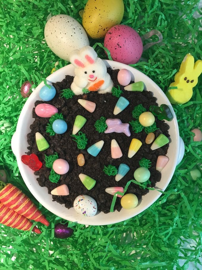 A bowl full of cheesecake dip topped with crumbled Oreos and Easter candy.