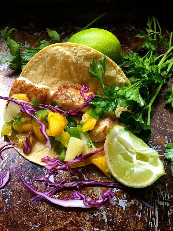 A flour tortilla with fish, cut-up mangos, and other vegetables. 