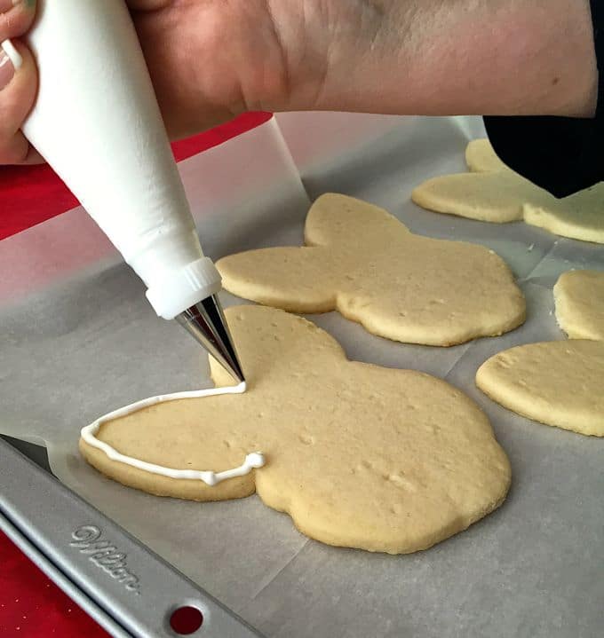 Edging the sugar cookies in white using thick icing in a piping bag.