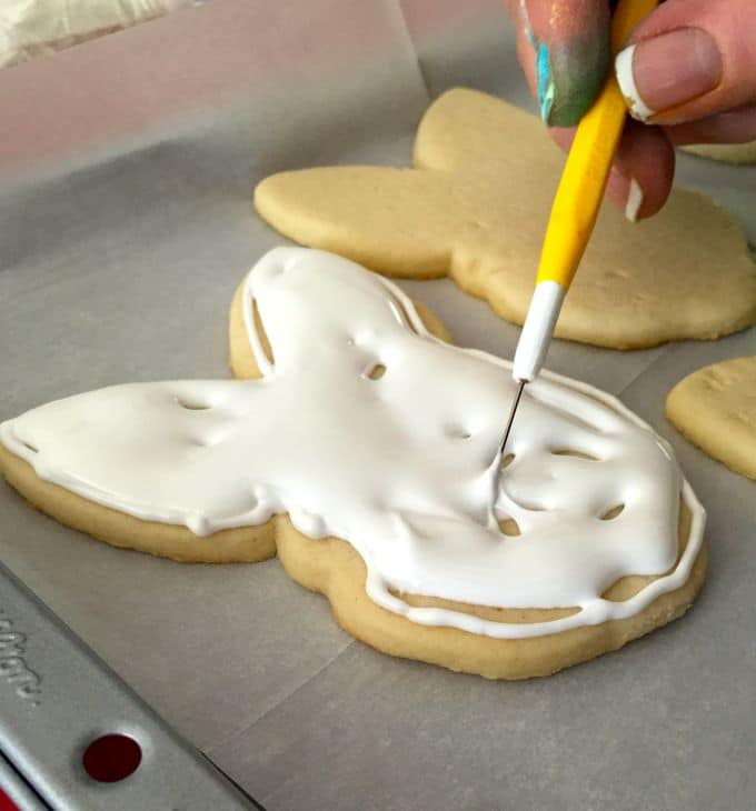 Evenly spreading and filling the space inside the piped edging with thin white icing. 