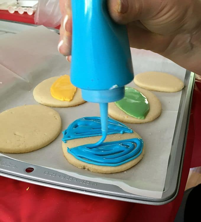Sugar cookies on a baking sheet topped with different colored icing. 