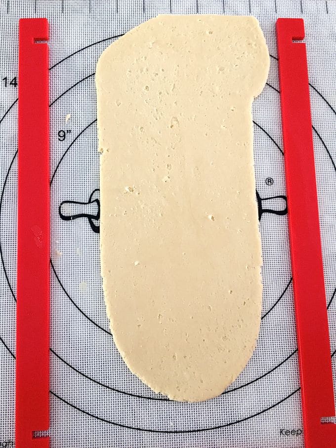 Strip of rolled cookie dough on a pastry mat with two red guide sticks.