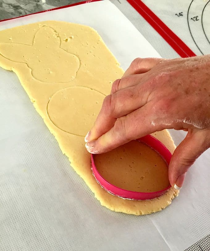 Cutting out rolled cookie dough with a round cookie cutter.