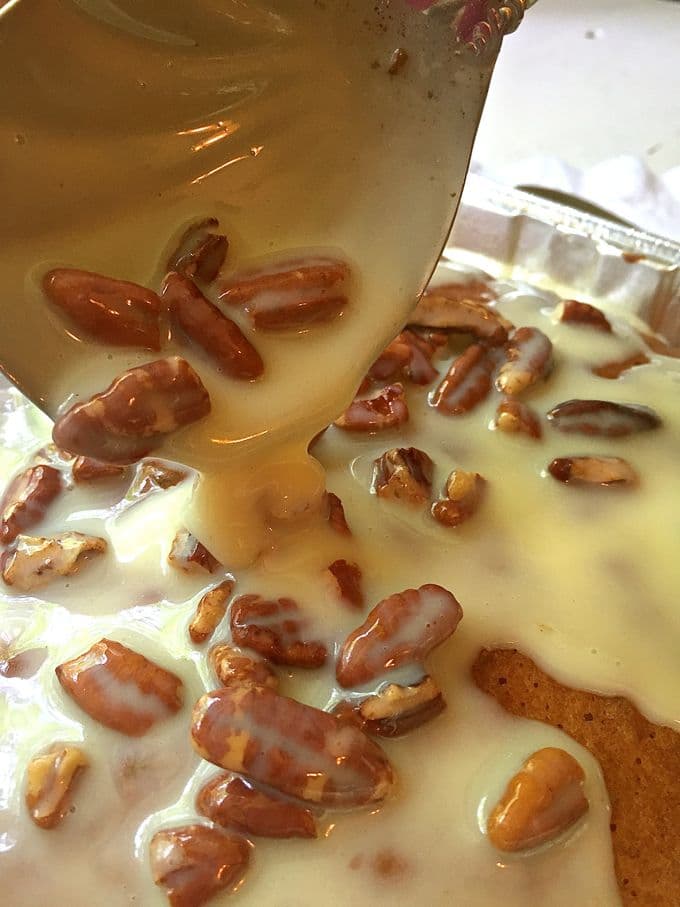 Praline and pecan topping being spooned over a sheet cake. 