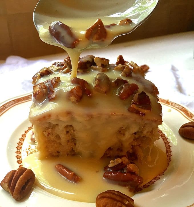 A piece of cake on a saucer with a creamy sauce with pecans on top. 