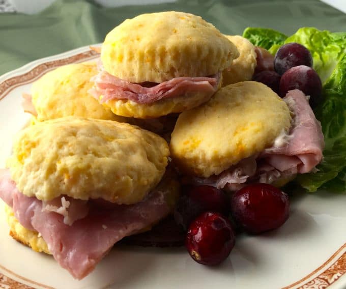 Plate filled with sweet potato biscuits with country ham garnished with cranberries and lettuce.