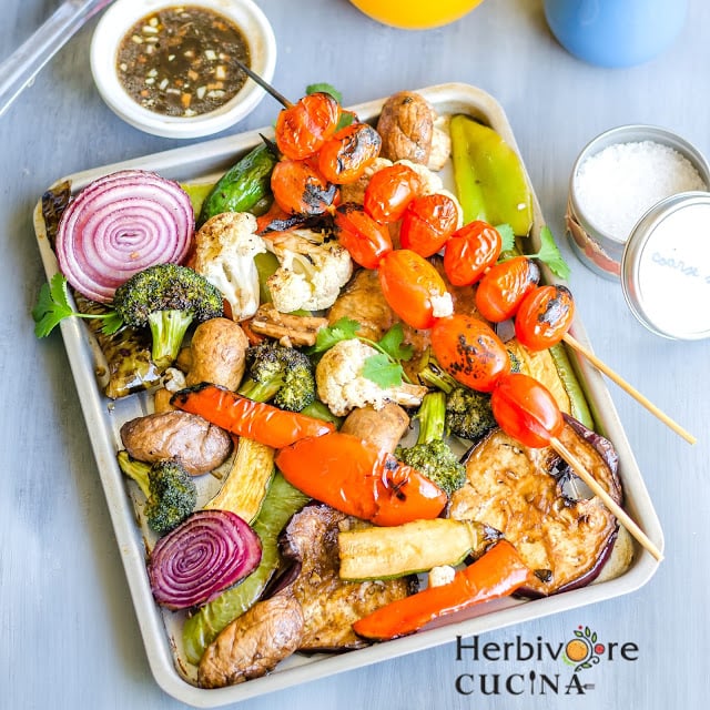 A sheet pan full of an assortment of grilled vegetables and two skewers with cherry tomatoes.