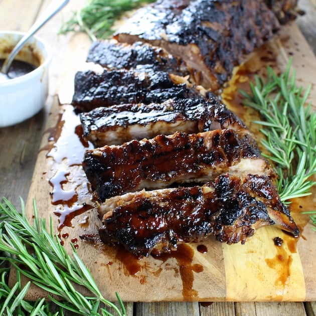 A slab of balsamic baby back ribs on a cutting board garnished with sprigs of rosemary.