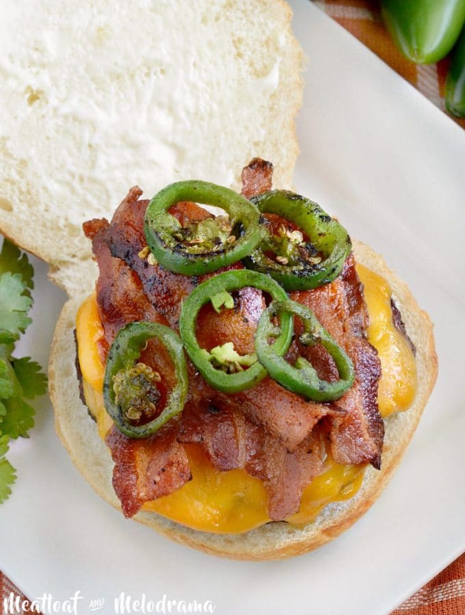 A hamburger on a bun topped with jalapeno slices, cheese and bacon.