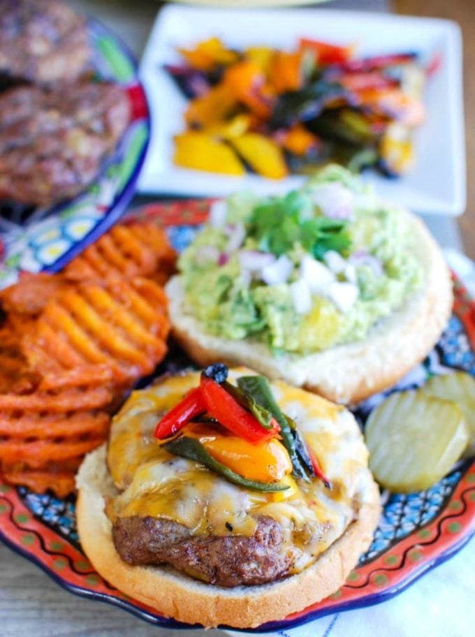 A hamburger on a bun topped with guacamole and peppers.