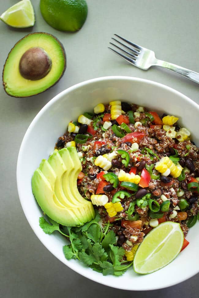 A white bowl full of quinoa salad and topped with avocado slices and a lime slice.