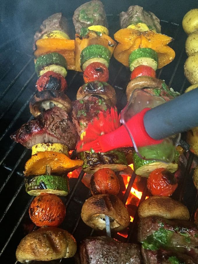 Basting Steak Shish Kabobs with chimichurri sauce while cooking on the grill.
