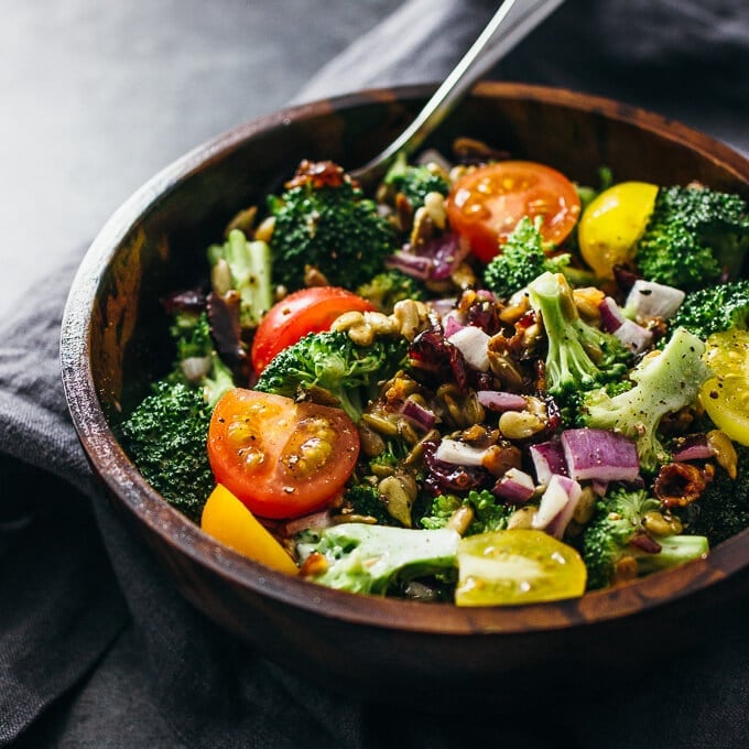 A wooden bowl of broccoli salad with tomatoes and red onions.