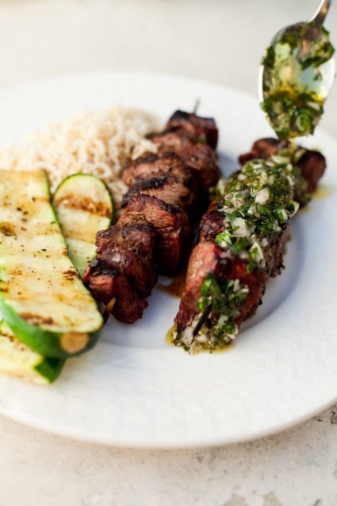 Two beef kabobs on a white plate with rice and grilled zucchini.