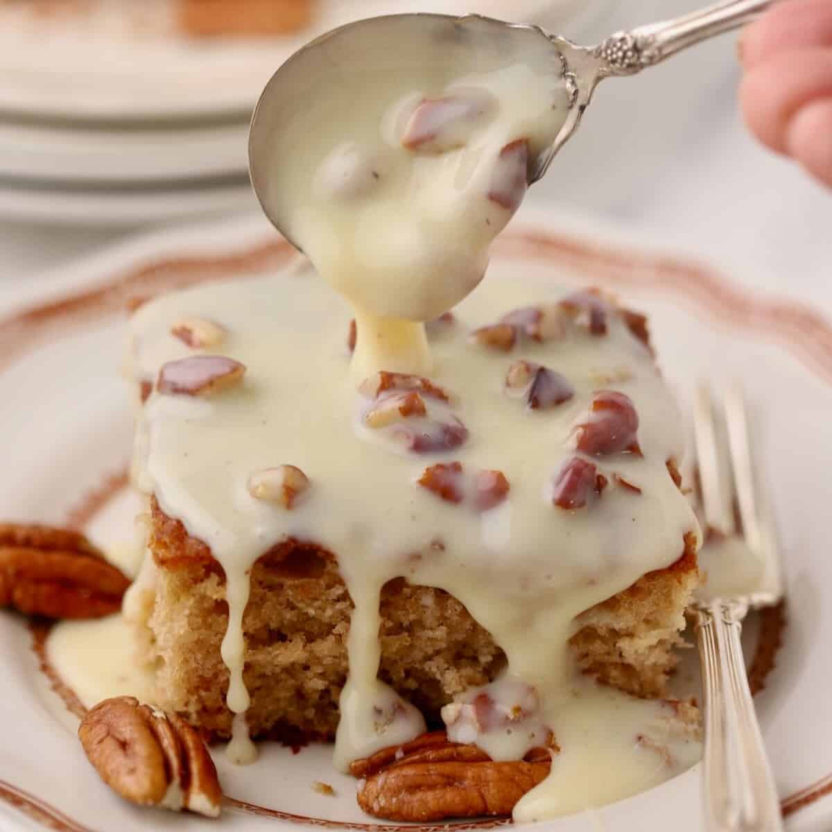 Southern Pecan Praline Cake on a plate with topping being spooned over it.