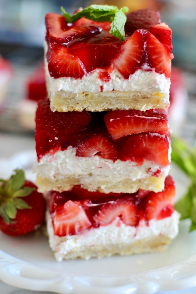 A stack of three delicious looking strawberry cheesecake bars on a plate.
