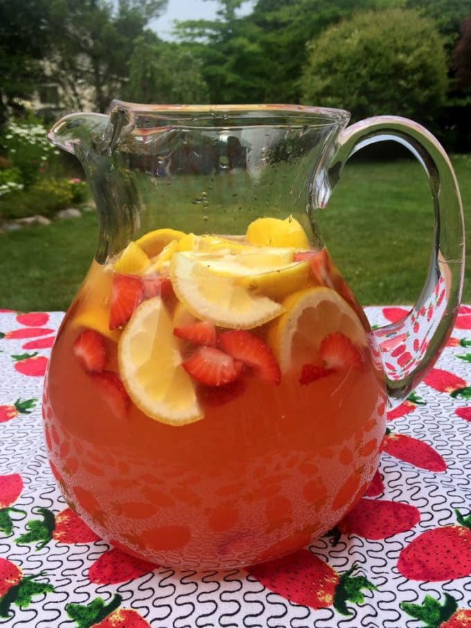 A large pitcher of strawberry lemonade with slices of lemons and strawberries.