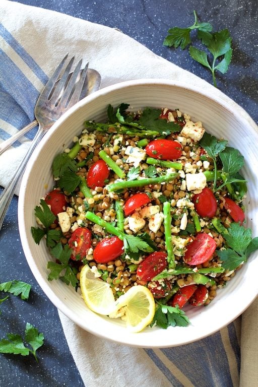 Lentils, Asparagus, and Tomato Salad with Feta Cheese in a white bowl on top of a blue and white napkin.