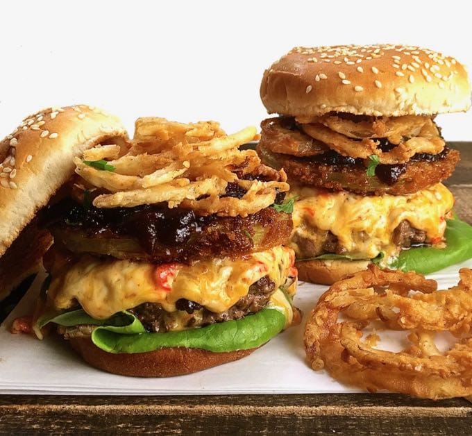 Ultimate Southern Style Burgers with the top of the bun removed showing onion rings, fried green tomatoes and melted pimento cheese