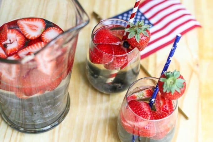 Glasses with red, white and blue sangria, topped with sliced strawberries. A great 4th of July recipe.