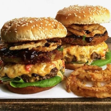 Two hamburgers topped with pimento cheese, fried onion rings, and a fried green tomato.