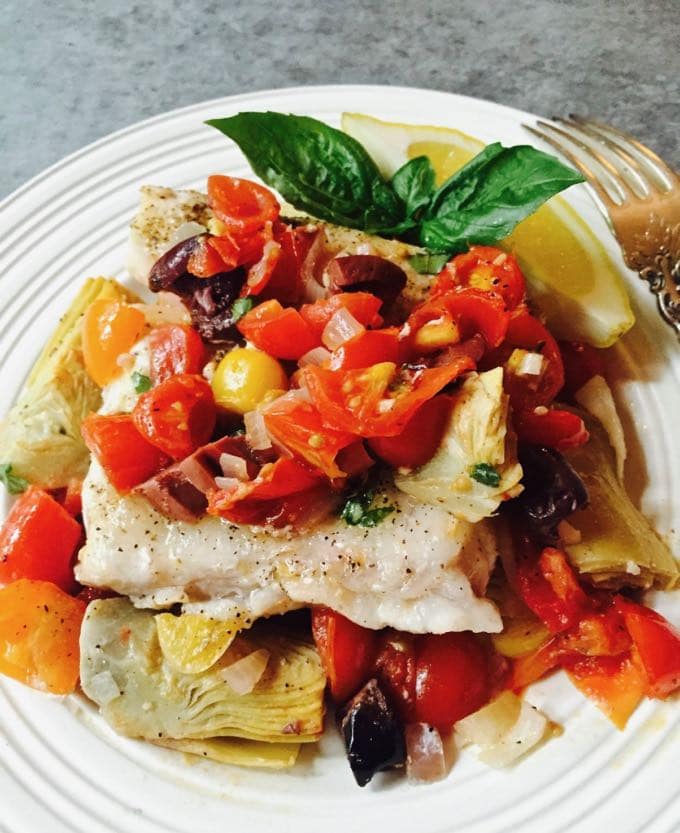 Tasty Baked Grouper with Tomatoes and Artichokes on a white plate, garnished with fresh basil. 