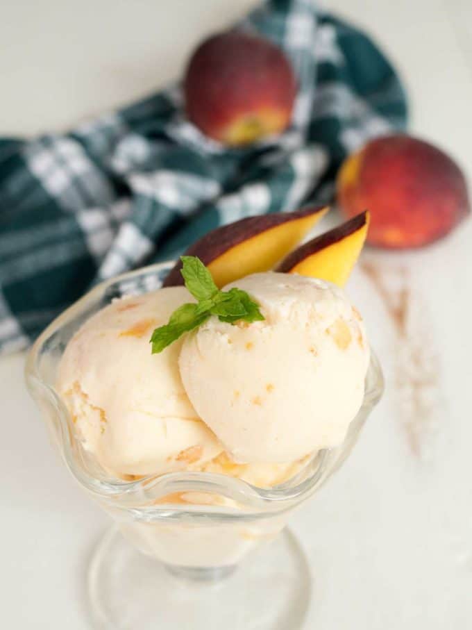 Two scoops of peach ice cream in a glass dessert dish. 