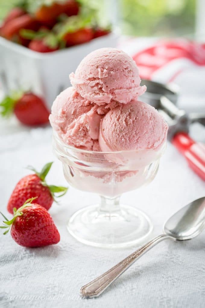 Fresh Strawberry Ice Cream in a clear glass dish next to some fresh strawberries. 