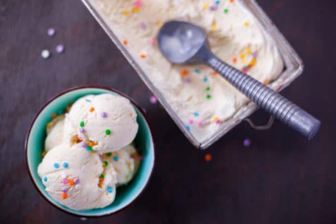 Scoops of Cake Batter Ice Cream in a blue bowl next to a container with a ice cream scoop. 