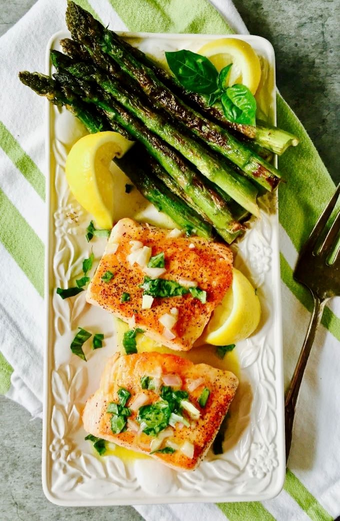 A serving platter with two pan-seared salmon fillets, asparagus and lemon slices. 