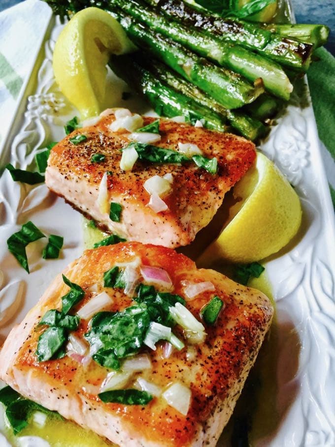 Pan Seared Salmon with Asparagus on a white serving dish topped with parsley, lemon juice and shallots. 