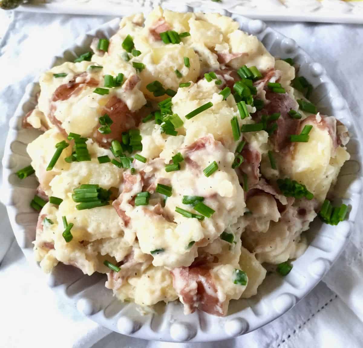 A white bowl with smashed potatoes topped with a sauce and chives.