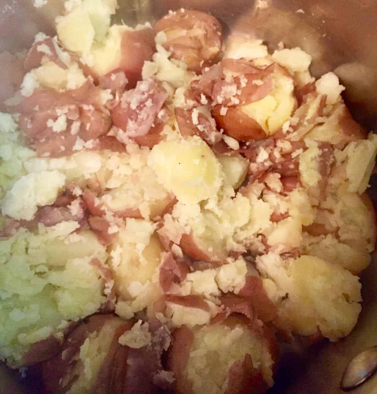 Smashed cooked unpeeled potatoes in a bowl.